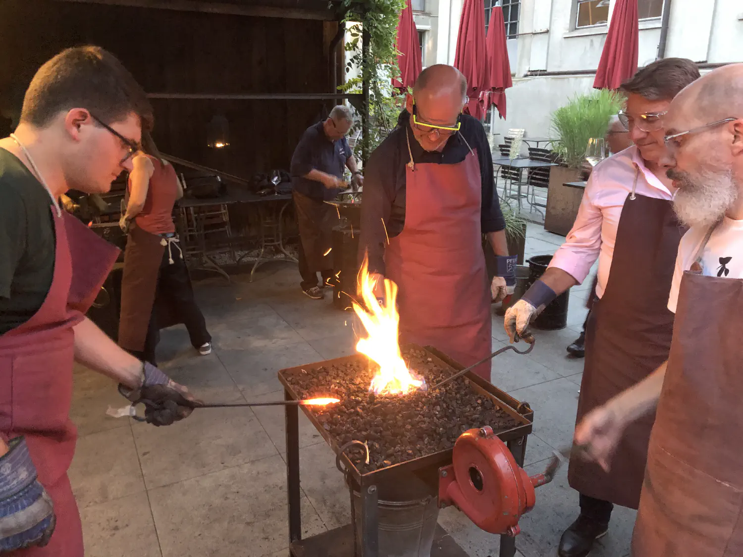 Vier Personen stehen verteilt um ein Kohlefeuer und erhitzen ihr Werkstück zur Bearbeitung.